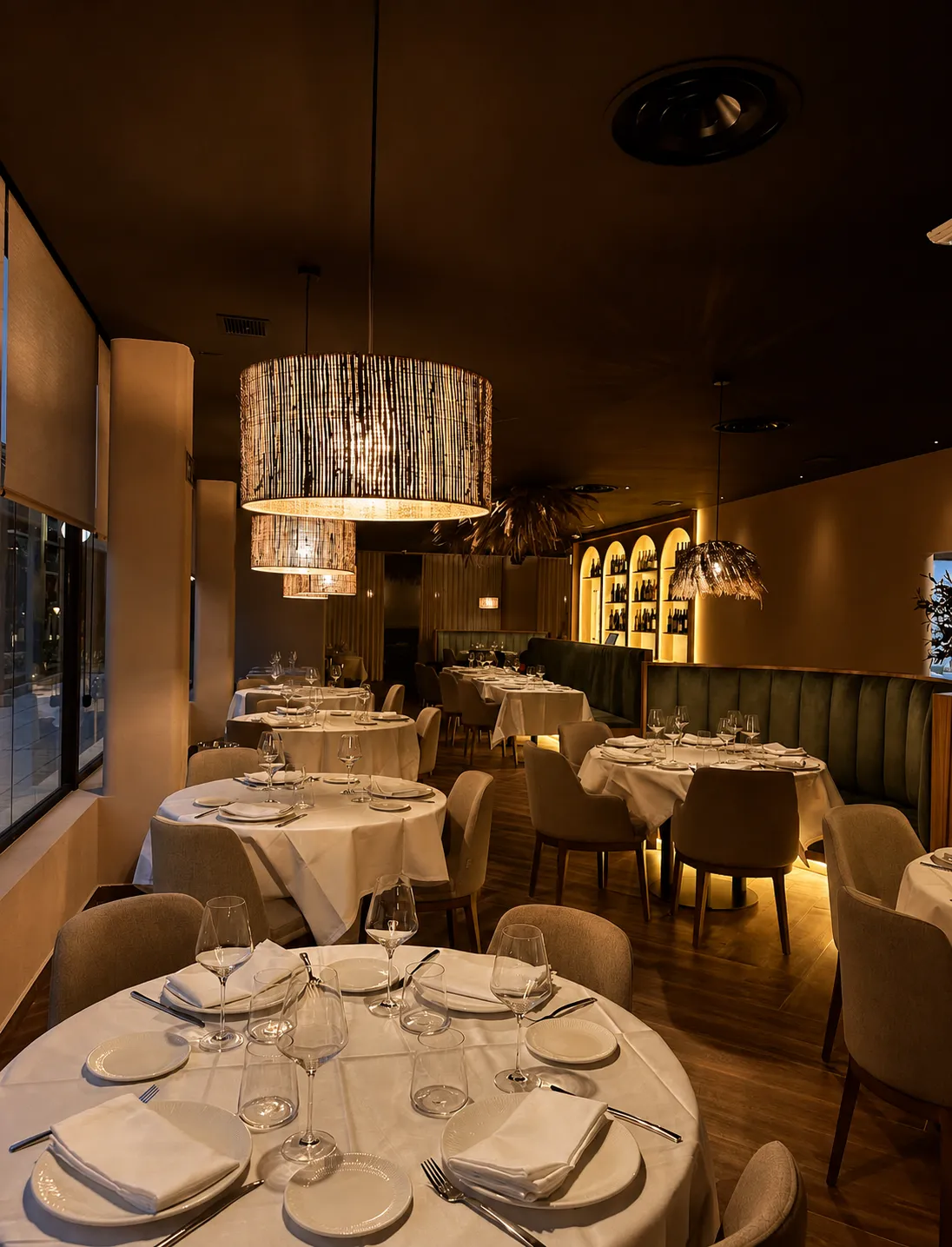 Comedor con mesas vestidas de blanco, lámparas de fibra y banco de terciopelo verde